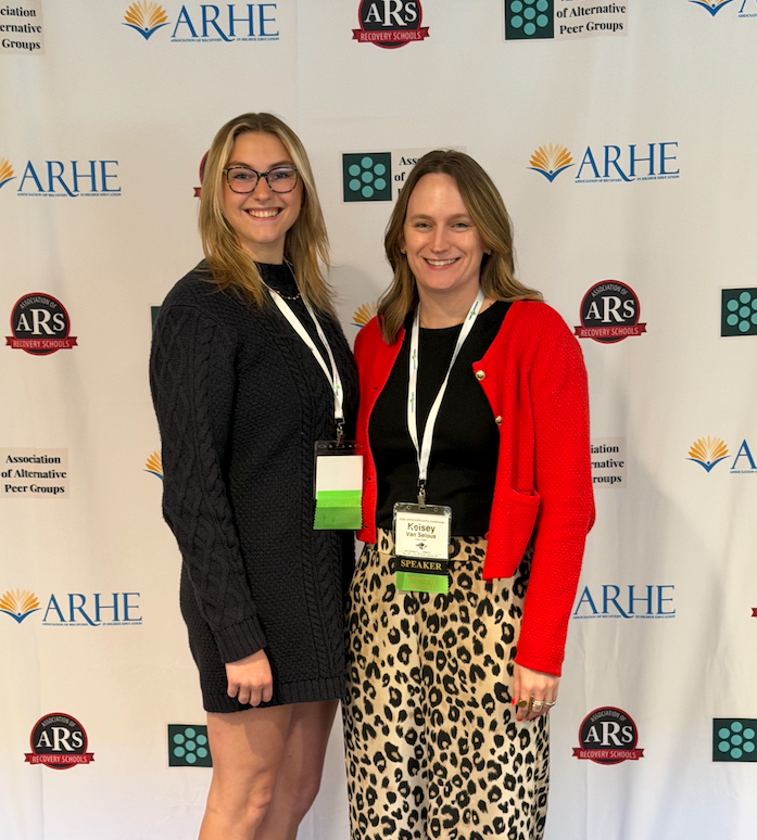 Carly and Kelsey pose in front of the backdrop at ARHE conference