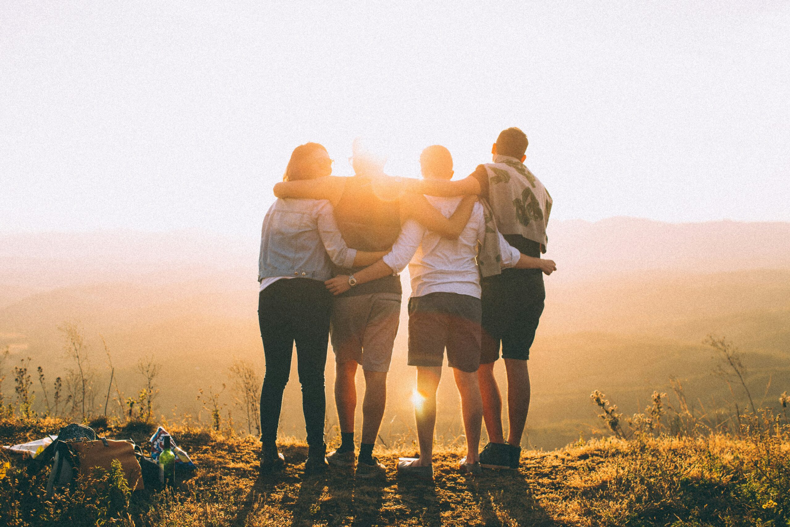People stand with their arms around each other facing the sunset outdoors