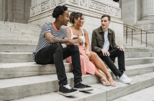 Three young people sit on the steps of a large white building