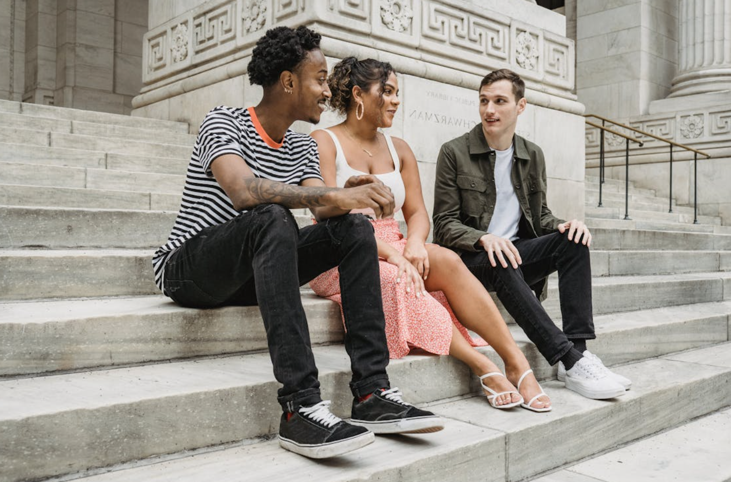 Three students sit and chat on concrete steps of a large building