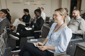 A woman smiles and sits in the audience at a conference