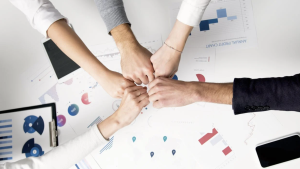 Five hands fist bumping over a desk with data papers on it