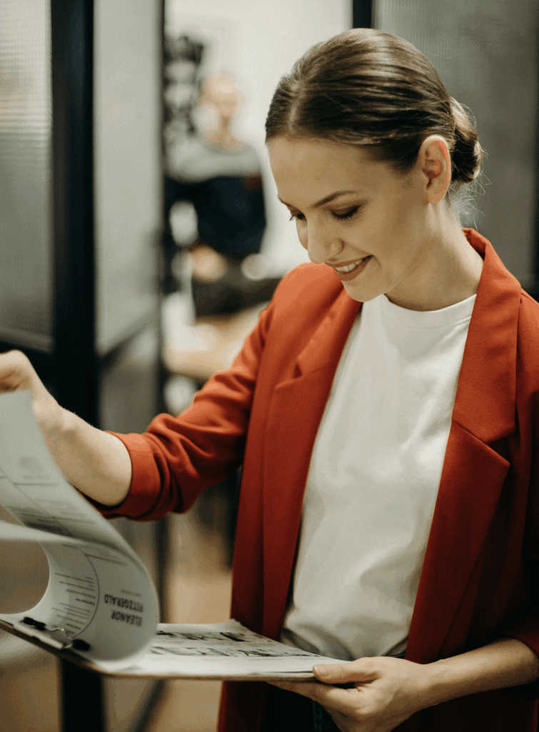 Woman in red jacket stands and smiles down at a clipboard