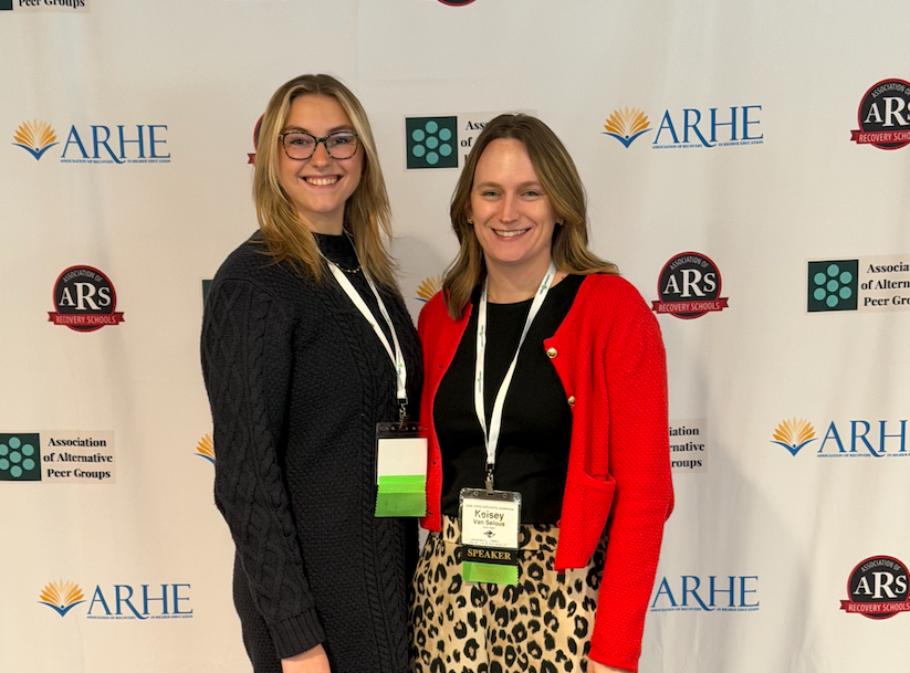 Carly and Kelsey pose in front of the backdrop at ARHE conference